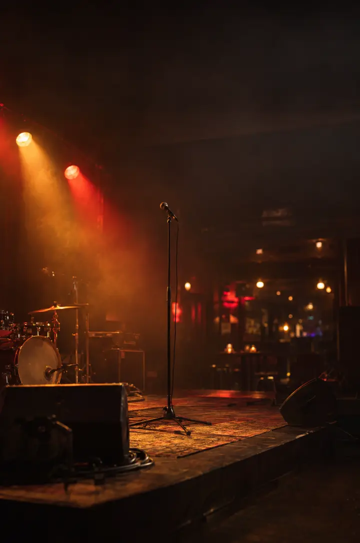An empty club stage at night, amber and deep red lights cutting through haze, a lone microphone stand at center.